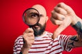 Handsome detective bald man with beard using magnifying glass over red background with angry face, negative sign showing dislike
