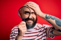 Handsome detective bald man with beard using magnifying glass over red background stressed with hand on head, shocked with shame