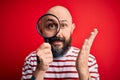 Handsome detective bald man with beard using magnifying glass over red background very happy and excited, winner expression