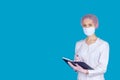 A handsome doctor in a medical mask, cap and gloves with a Notepad in his hands on a blue background. Royalty Free Stock Photo