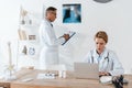 handsome doctor standing near x-ray and attractive colleague using laptop. Royalty Free Stock Photo