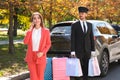 Handsome driver with shopping bags and young businesswoman near car