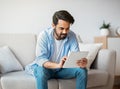 Handsome Eastern Guy Using Digital Tablet While Relaxing On Couch At Home Royalty Free Stock Photo