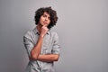 Handsome eastern mindful student holding hand on his chin while thinking, standing against gray wall Royalty Free Stock Photo