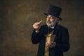 Handsome elderly gray-haired man, gentleman, aristocrat or actor eating fast food isolated on dark vintage background Royalty Free Stock Photo