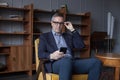 Handsome elderly grey haired successful businessman in glasses looking on his mobile phone, sitting in office Royalty Free Stock Photo