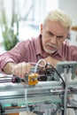 Handsome elderly man adjusting extruder of 3D printer