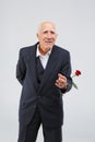 A elderly man in a black suit, smiling and holds one red rose behind him. Isolation. Royalty Free Stock Photo