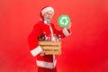 Handsome elderly man with gray beard wearing santa claus costume holding box with plastic bottles and showing green recycling sign Royalty Free Stock Photo