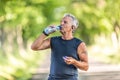 Handsome elderly man rehydrates after a run outdoors in the nature by drinking water from a bottle Royalty Free Stock Photo
