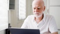 Handsome elderly senior man working on laptop computer at home. Remote freelance work on retirement Royalty Free Stock Photo