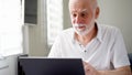 Handsome elderly senior man working on laptop computer at home. Remote freelance work on retirement Royalty Free Stock Photo