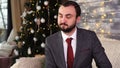 Handsome businessman nods in dissenting near christmas tree in cozy room with holidays decorations