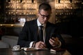 Handsome elegant businessman sitting at modern restaurant checking his smart phone and making the notes