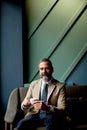 Handsome elegant serious businessman sitting in armchair and holding cup of espresso. Royalty Free Stock Photo