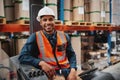 Handsome engineer wearing protective uniform and hardhat smiling joyfully to the camera sitting in forklift stacker