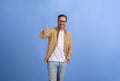 Handsome entrepreneur smiling ecstatically and showing thumbs up while posing over blue background