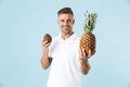 Handsome excited happy adult man posing  over blue wall background holding coconut and pineapple Royalty Free Stock Photo