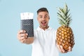 Handsome excited happy adult man posing isolated over blue wall background holding passport and pineapple Royalty Free Stock Photo
