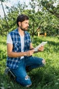 handsome farmer squatting holding tablet in apple garden at farm