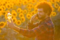 Handsome farmer standing in the middle of a golden sunflower field smiling and talking on phone while holding up a sunflower oil Royalty Free Stock Photo