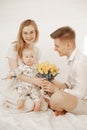 Handsome father gift little baby and mother bouquet of yellow tulips sitting on bed on white background. Home family Royalty Free Stock Photo