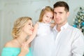 Handsome father keeping little daughter and young mother kissing hand near Christmas tree.