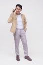 A handsome FIlipino guy in a khaki jacket, white shirt and light gray pants. Holding a phone talking to someone. Whole body photo Royalty Free Stock Photo
