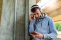 Handsome fit man taking a break after intensive training outdoors, texting on his smart phone wearing headphones Royalty Free Stock Photo