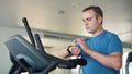 Handsome fit young man in gym doing exercises on exercise bike. Using his smartwatch checking vitals