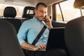 Businessman using laptop talking on smartphone while going by car Royalty Free Stock Photo