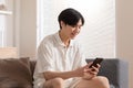 Handsome Freelancer Asian young man sit on couch looking on mobile screen recieved good news raise hand up celabrating. Happiness Royalty Free Stock Photo