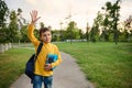 A handsome friendly charming schoolboy 9 years old, in the park, with a backpack on one shoulder and notebooks in his hands, waves Royalty Free Stock Photo