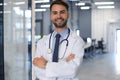Handsome friendly young doctor on hospital corridor looking at camera, smiling Royalty Free Stock Photo