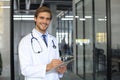 Handsome friendly young doctor on hospital corridor looking at camera, smiling Royalty Free Stock Photo