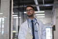 Handsome friendly young doctor on hospital corridor looking at camera, smiling Royalty Free Stock Photo