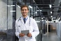 Handsome friendly young doctor on hospital corridor looking at camera, smiling Royalty Free Stock Photo