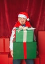 Handsome funny man wearing Santa hat holding heavy Christmas gift boxes on the red background. New Year style