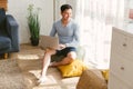 Handsome gay Asian man working with a laptop, sitting near the window in the living room at home. Good-looking LGBT man smiling, Royalty Free Stock Photo