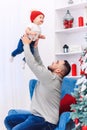 Handsome dad throwing up his amusing infant boy in the air near festive decorated christmas tree. Royalty Free Stock Photo