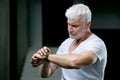 Gray haired senior man looking at sport watch at his hand. Sport and health care concept