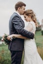 Handsome groom embracing beautiful bride and kissing her on the forehead, happy newlyweds portrait, couple hugging outdoors Royalty Free Stock Photo