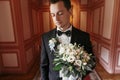 Handsome Groom holding stylish bouquet in the morning in the luxury room. sensual  man portrait in suit with flowers in luxury Royalty Free Stock Photo