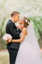 Handsome groom hugging beautiful bride with bouquet in romantic european park Royalty Free Stock Photo