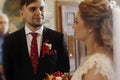 Handsome groom looking at beautiful bride, happy groom in stylish black suit glancing at gorgeous blonde bride in church during w Royalty Free Stock Photo