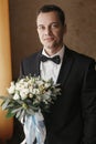 Handsome Groom portrait with stylish wedding bouquet for bride in the morning in the room. man hands holding flowers, standing at Royalty Free Stock Photo