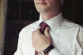 Handsome groom preparing for wedding, putting on tie