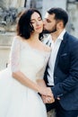 Handsome groom is softly kissing the gorgeous bride in the cheek. Sensual outdoor portrait. Royalty Free Stock Photo