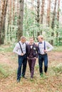 Handsome groom with stylish groomsmen walking in the forest and having fun on a wedding day.