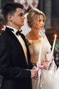 Handsome groom in suit and a beautiful blonde bride holding candles in church close-up Royalty Free Stock Photo